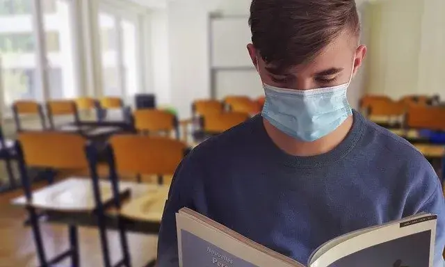 Un estudiant amb mascareta agafa un llibre en una classe.