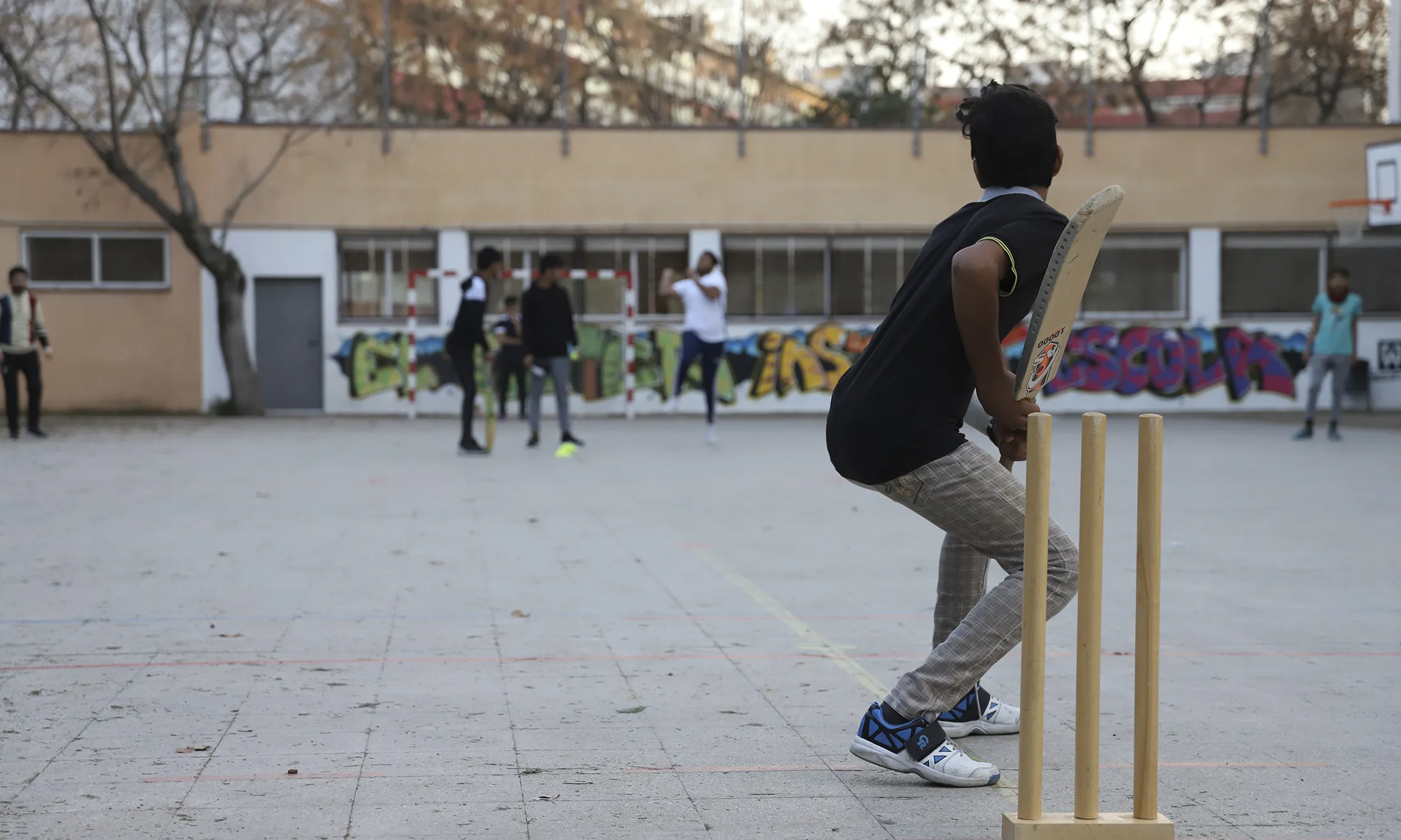 Joves jugant al criquet al pati d'una escola