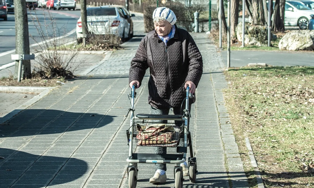 Una persona amb Alzheimer camina pel carrer amb un caminador.
