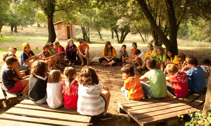 Un grup d'infants asseguts en rotllana damunt d'uns palés. 