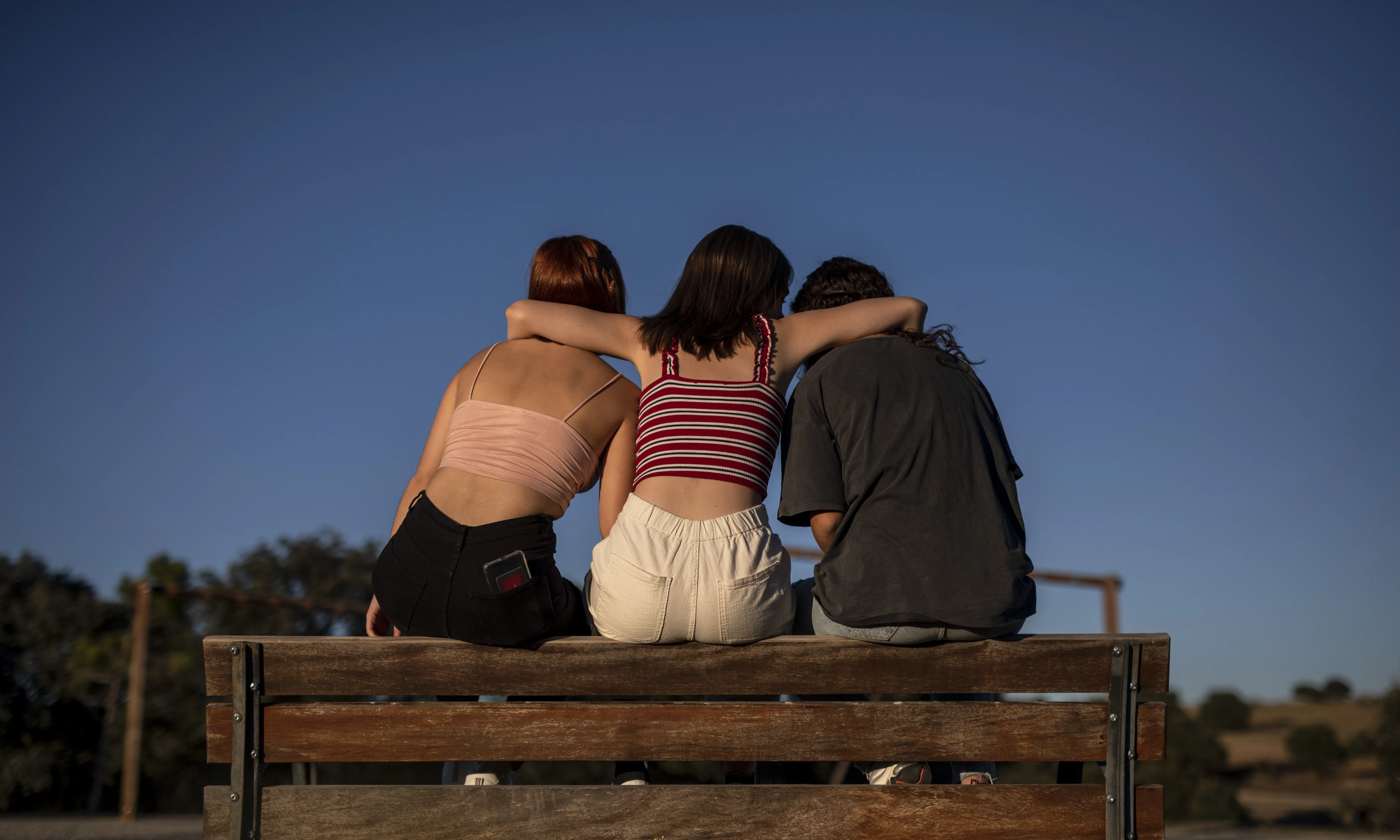 Escena representada: tres noies seuen a un banc donant-se suport.