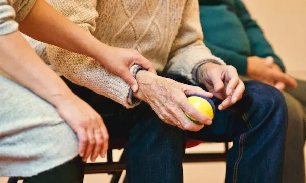 Cuidadora agafant la mà d'una persona gran que té una pilota. Font: Matthias Zomer