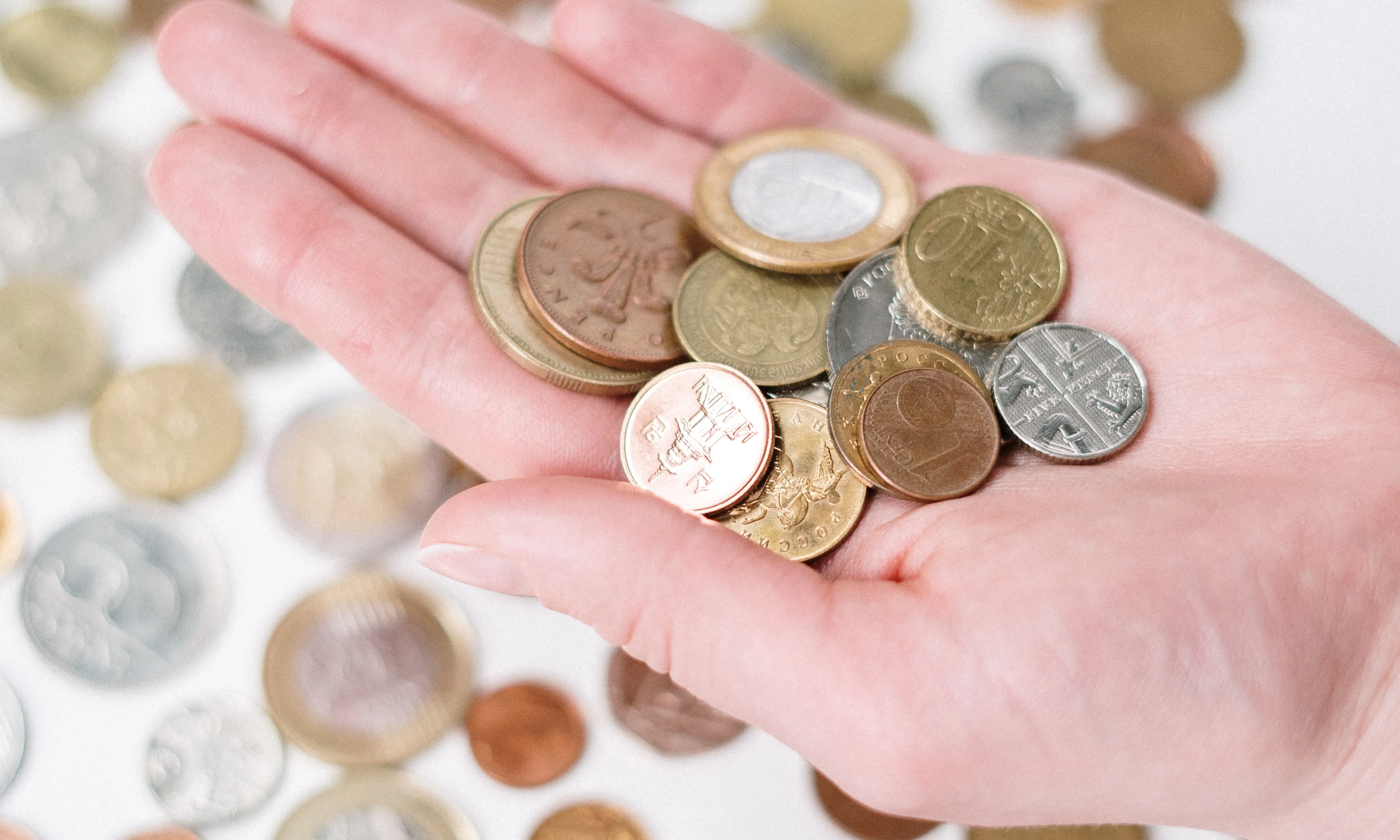 Taula amb monedes d'Euro i mà agafant-n'he. Font: Pexels - cottonbro studio