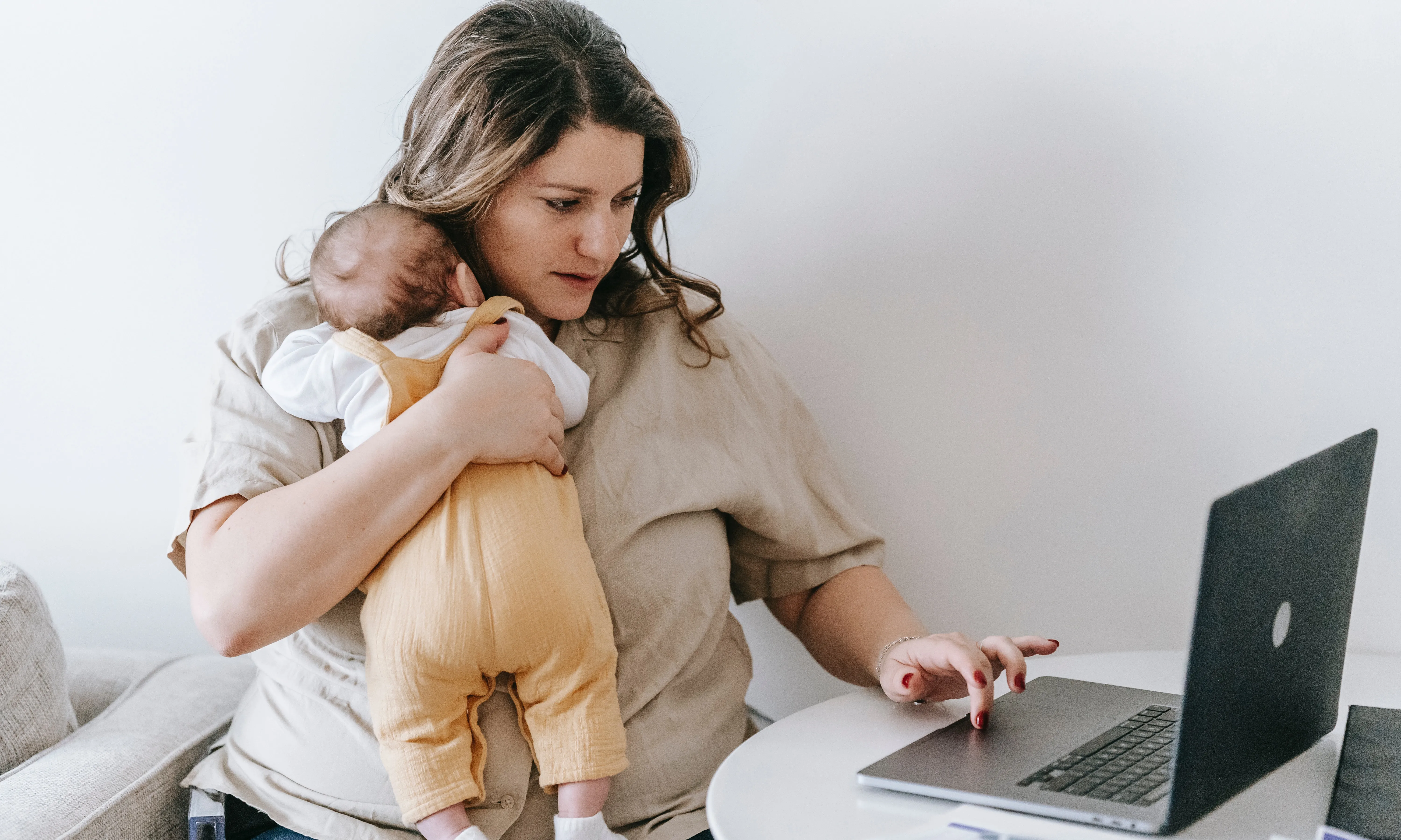 Dona amb un nadó en braços i escrivint a l'ordinador. Font: Pexels - Sarah Chai
