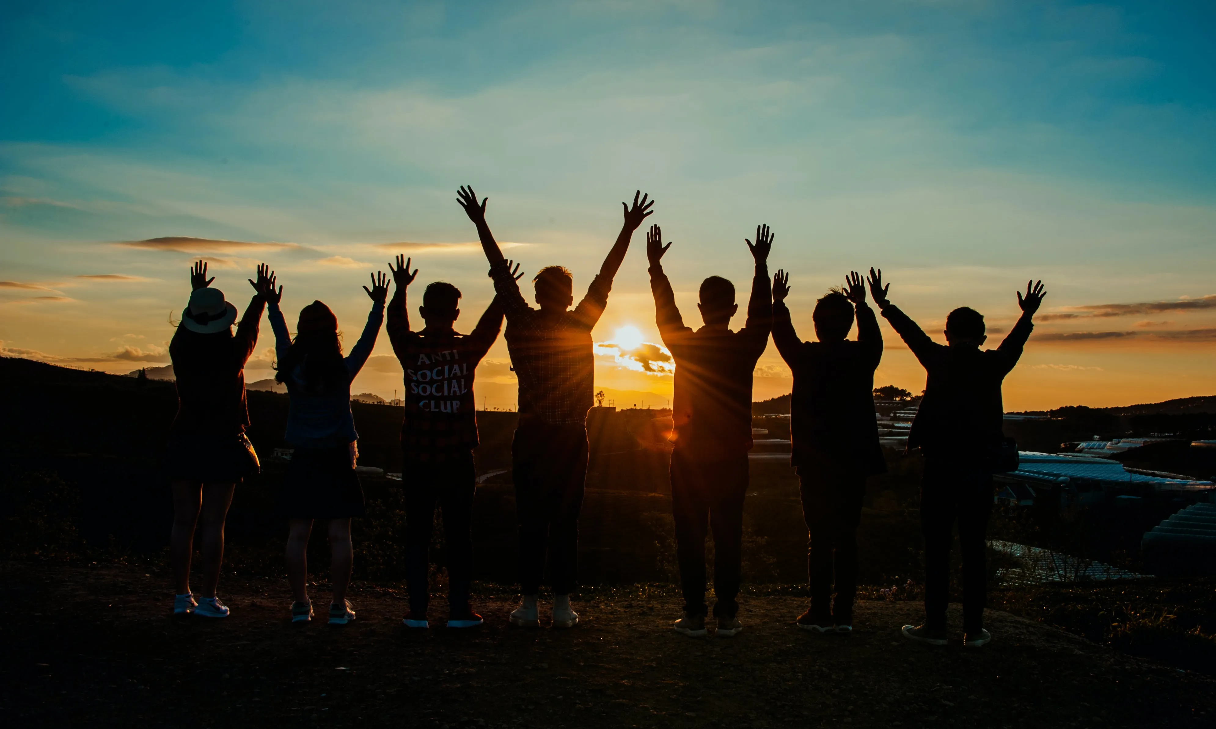 Persones amb mans alçades mirant el sol. Font: Pexels - Min An