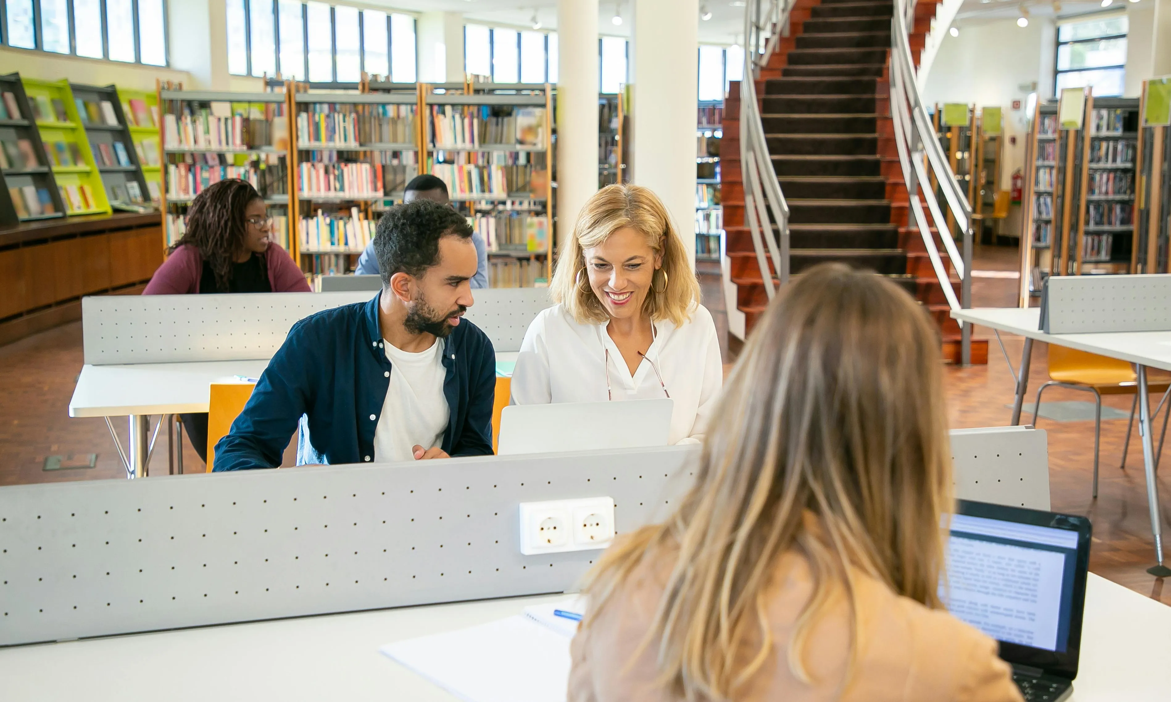 Persones aprenent a fer servir un ordinador en una biblioteca. Font: Pexels - Kampus Production