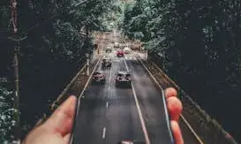 Mà amb un mòbil que es fa extensiu a una carretera amb arbres als laterals