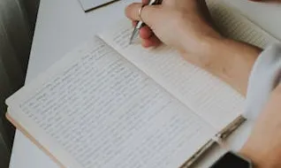Persona escrivint Persona en un escriptori escrivint a mà en una llibreta
