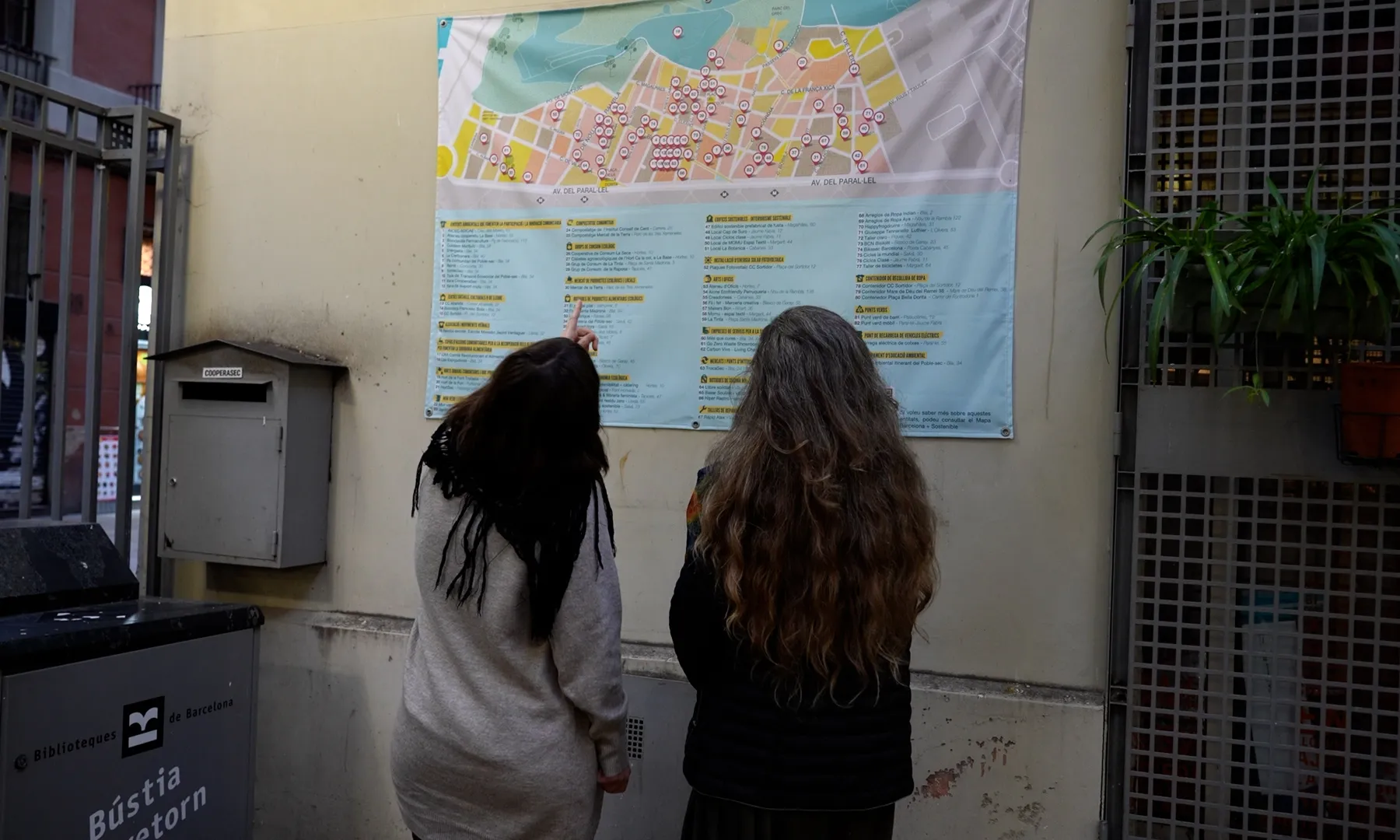 Dues dones, la Gemma i la Chiara, miren un mapa gegant del barri del Poble-sec que hi ha a la paret.