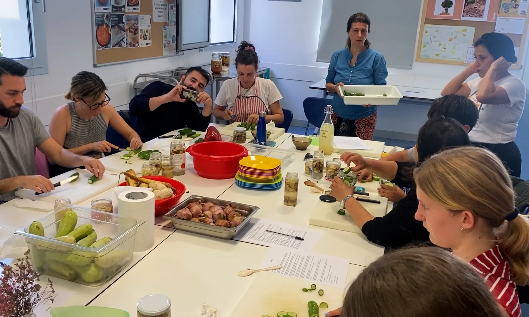 Un grup de persones assegudes al voltant d'una taula fent un taller de cuina, preparant envinagrats.