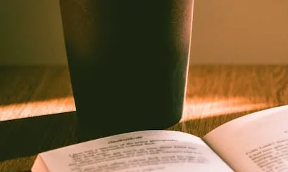 Taula amb un llibre obert i una planta al fons