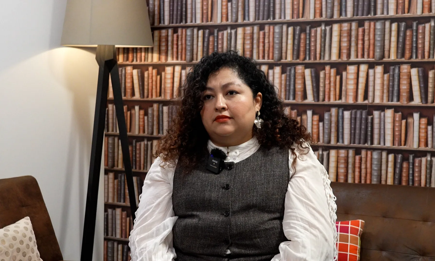 Retrat de l'Angélica Cárcamo, asseguda en una cadira amb una estanteria plena de llibres de fons.