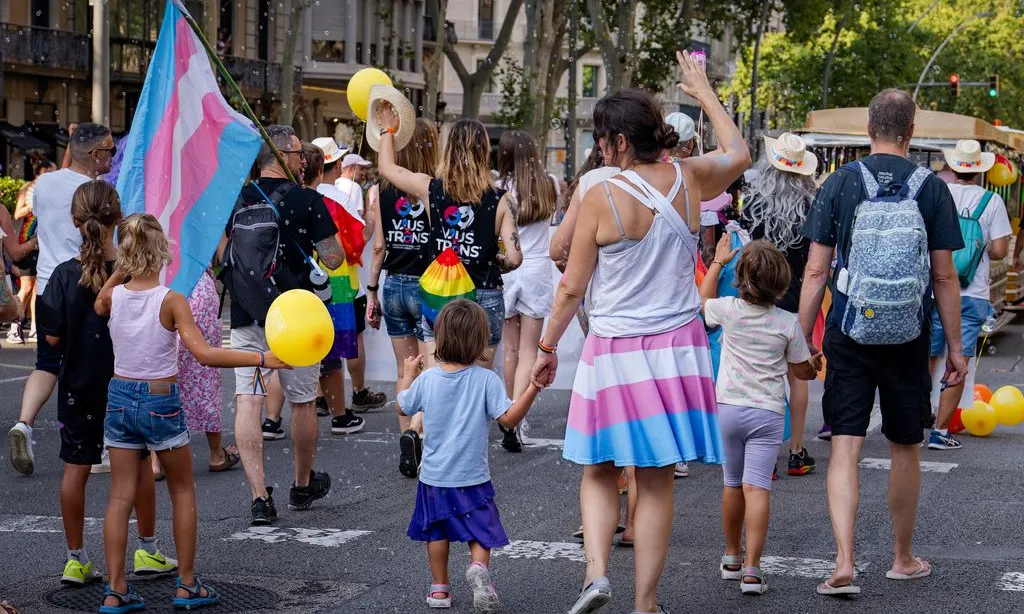 Famílies en una manifestació de l'Orgull LGTBI a Barcelona. S'observa la bandera trans a les faldilles d'una de les persones participants i enarbolada per una altra.