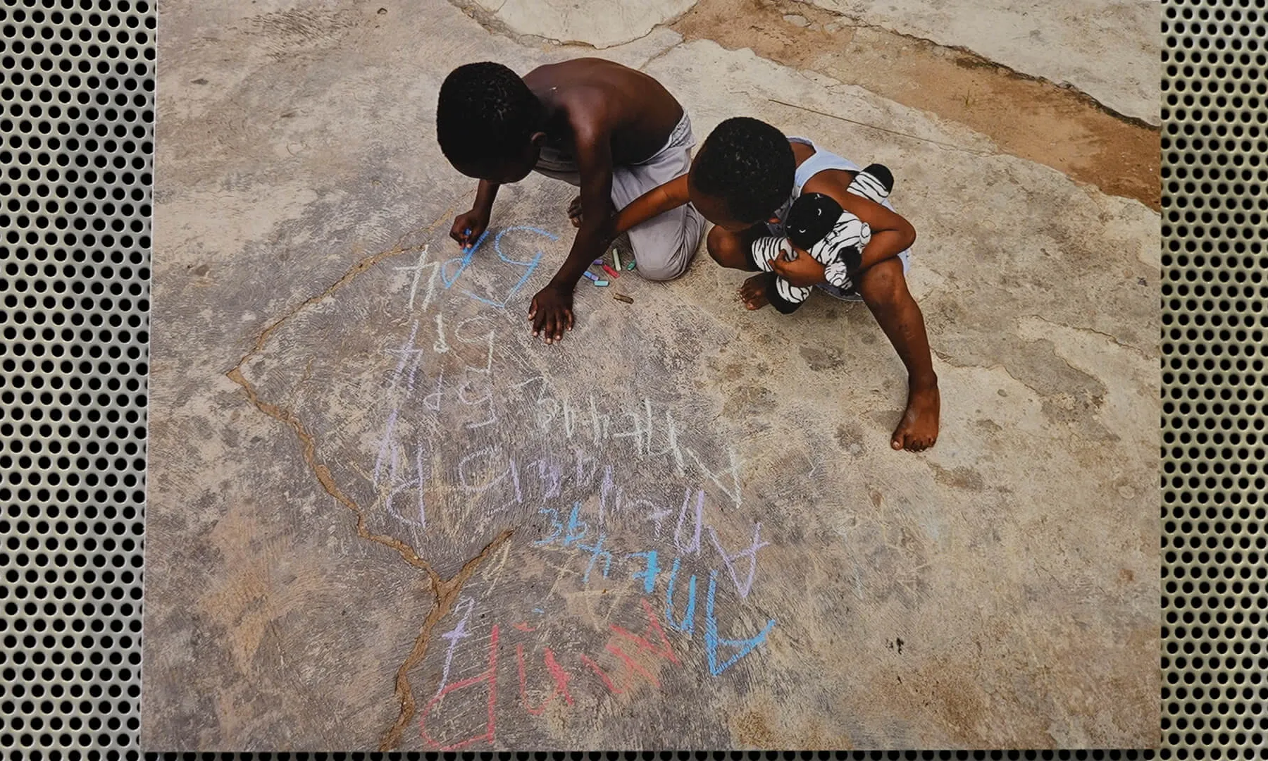 Una imatge de dos infants africans dibuixant amb guixos de colors el terra.