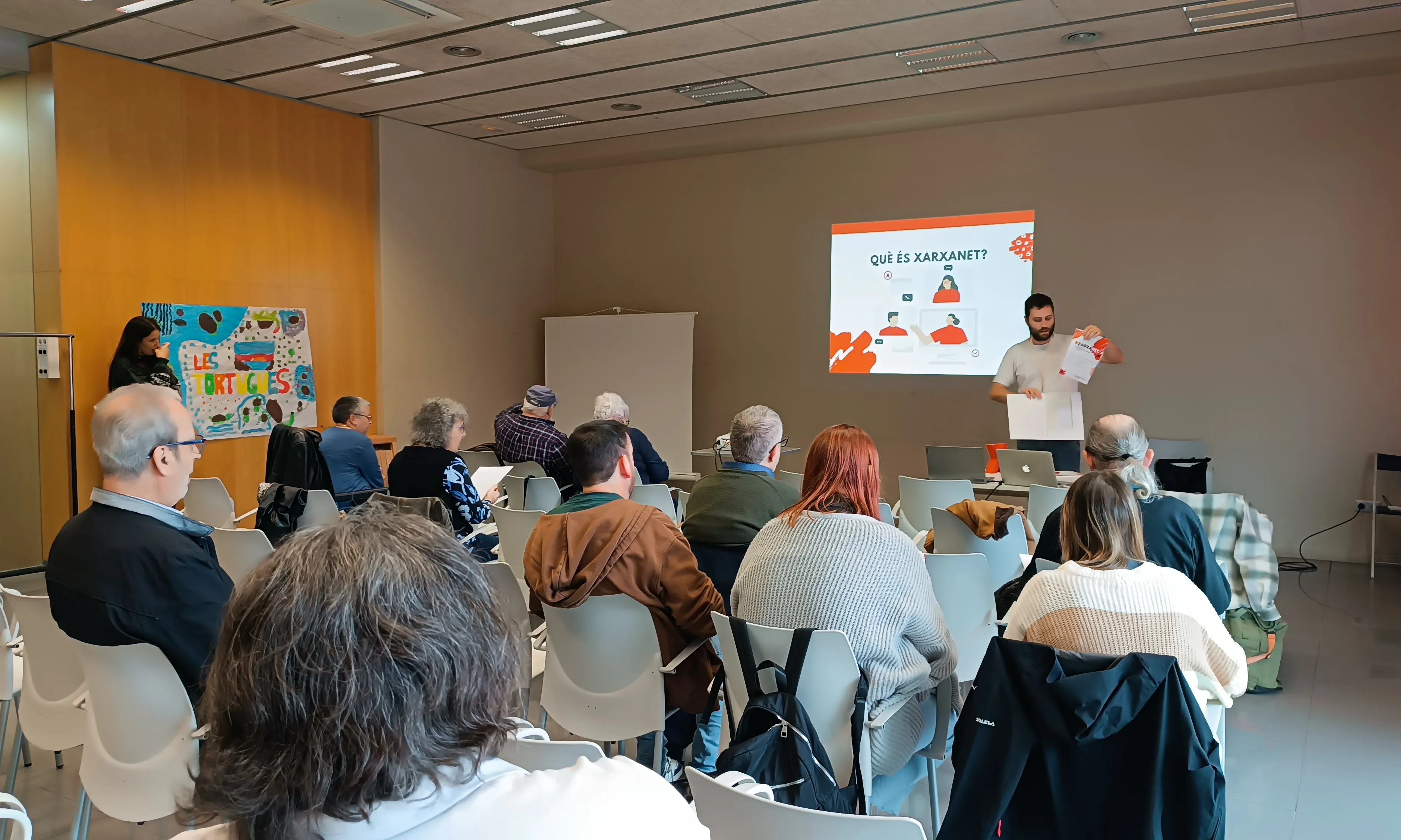 Un grup de persones assistint a una presentació per part d'un dels membres de Xarxanet, amb una imatge projectada al fons. 
