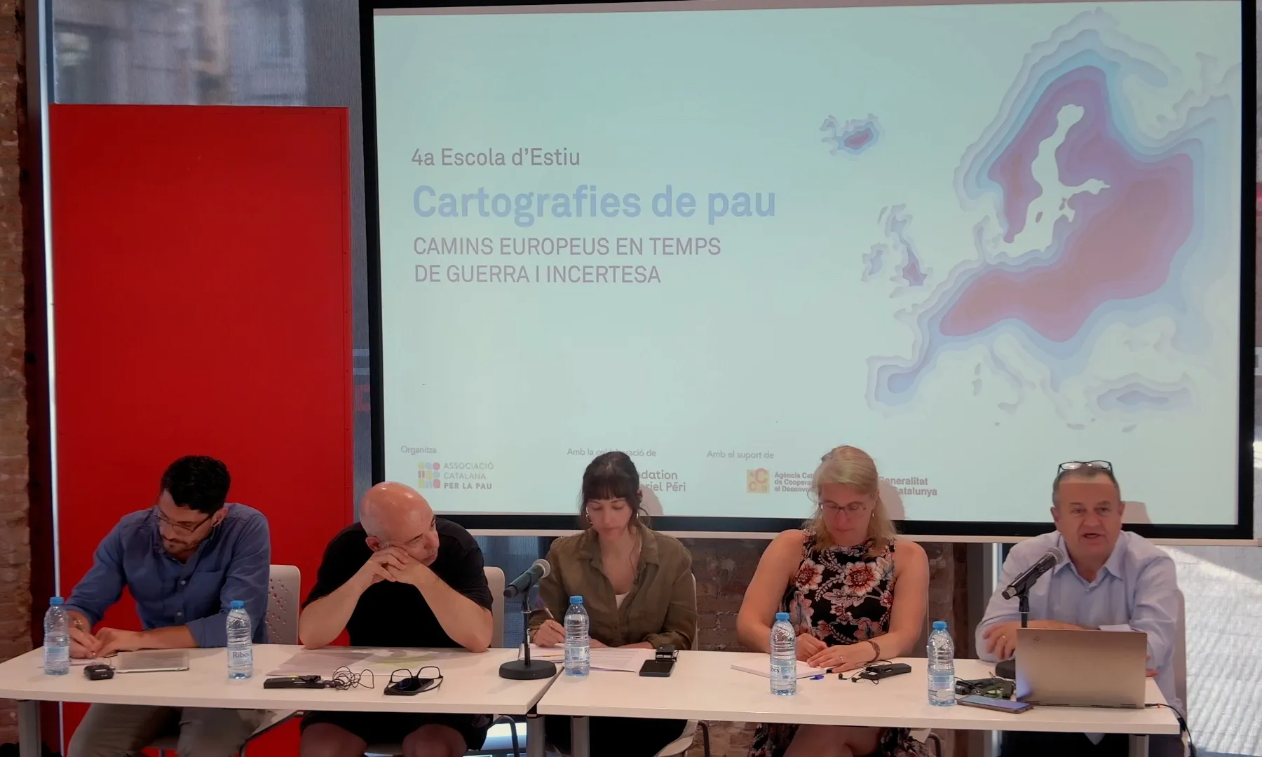 Diversos conferenciants asseguts en una taula donant un discurs, durant la 4a Escola d'Estiu de l'Associació Catalana per la Pau.