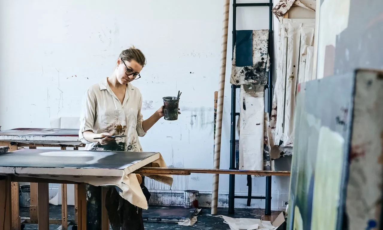 Una artista treballa en un gran llenç en un estudi, envoltada de material artístic.