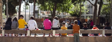 Nens de l'Escola Mercè Rodoreda asseguts en uns esglaons de la plaça de Nou Barris amb els apunts a les mans assistint a una classe. Font: Paula Jaume