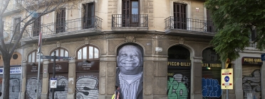 Una persona passa per davant del mural de Teo Vázquez en què retrata Juan Essomba, a carrer Marina de Barcelona, on ell va dormir tot un any. Font: Arrels Fundació