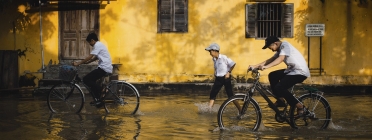 Nens en bicicleta en un carrer inundat per les pluges. Font: Llicència CC
