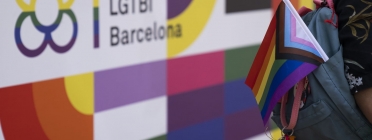 Cartell amb el logotip del Centre LGTBI de Barcelona amb una persona portant una bandera de l'arc de Sant Martí i trans enganxada a la motxilla. Font: Paula Jaume