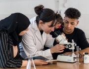Una professora amb dues alumnes que estan explorant a través d'un microscopi. Font: Niu d'Imatges de la Joventut
