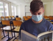 Un estudiant amb mascareta agafa un llibre en una classe. Font: Pixabay
