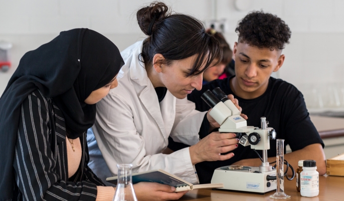 Una professora amb dues alumnes que estan explorant a través d'un microscopi. Font: Niu d'Imatges de la Joventut