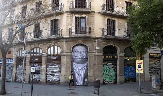 Una persona passa per davant del mural de Teo Vázquez en què retrata Juan Essomba, a carrer Marina de Barcelona, on ell va dormir tot un any. Font: Arrels Fundació