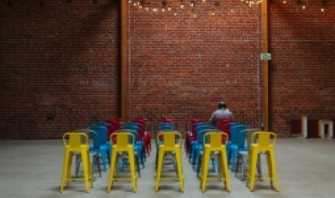 Files de cadires de diversos colors i una paret de totxos al fons. Font: Kyle Glenn