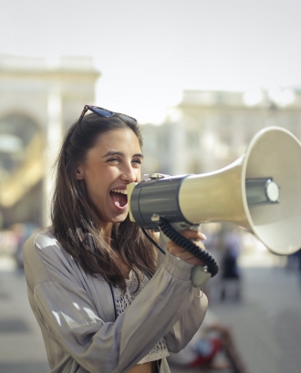 Noia cridant per un altaveu portàtil contenta. Font: Pexels - Andrea Piacquadi