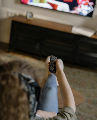 Persona amb un comandament a distància enfocant a una televisió. Font: Pexels - cottonbro studio