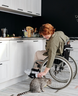 Persona en cadira de rodes a la cuina acariciant un gat. Font: Pexels - Marcus Aurelius