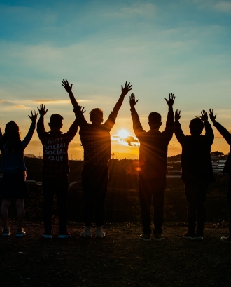 Persones amb mans alçades mirant el sol. Font: Pexels - Min An