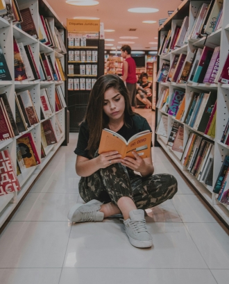 Noia llegint una revista a una biblioteca. Font: Pexels - Nicole Berro