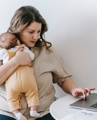 Dona amb un nadó en braços i escrivint a l'ordinador. Font: Pexels - Sarah Chai