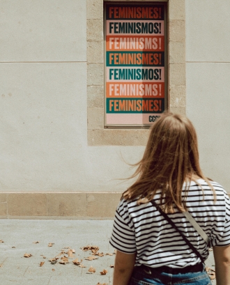 Noia mirant un cartell on posa feminisme en diferents idiomes. Font: Pexels - Sinitta Leunen