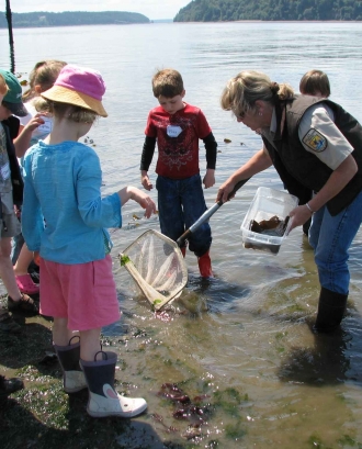 Nens escoltant i mirant a una educadora ambiental que està dins d'un llac